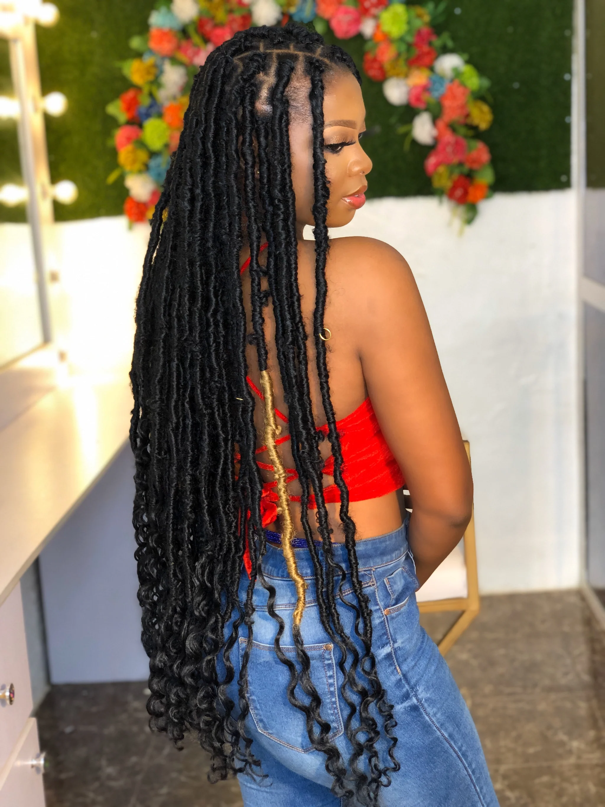 Woman with long goddess locs hairstyle in red top and blue jeans